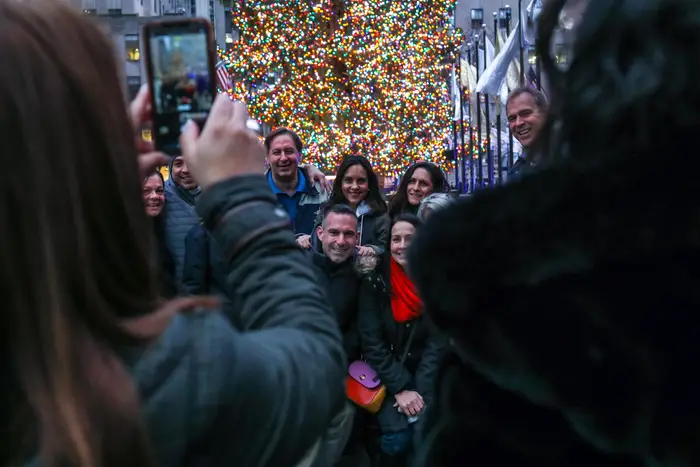 a group taking a photo in front of the rock center tree
